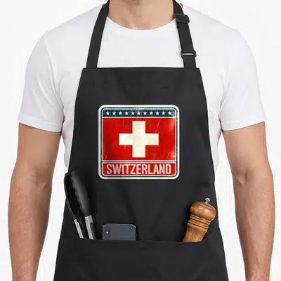 Tablier de cuisine noir avec un fanion Suisse rétro montrant une croix blanche, des étoiles et le mot Switzerland en bas.
