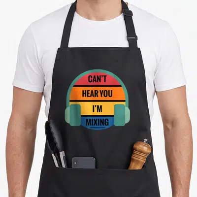 Tablier de cuisine noir avec illustration de casque audio coloré et texte Can't Hear You I'm Mixing en lettres noires sur bandes horizontales.