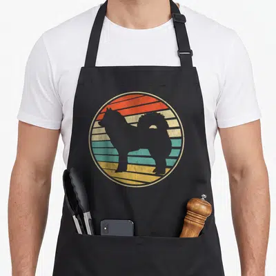Tablier de cuisine noir avec une illustration circulaire d'un chien Eurasier sur un fond de soleil rayé multicolore dans un style vintage.