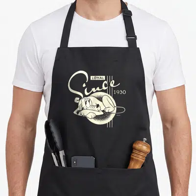Tablier de cuisine noir avec illustration rétro de Pluto et le texte Loyal Since 1930 en typographie blanche.