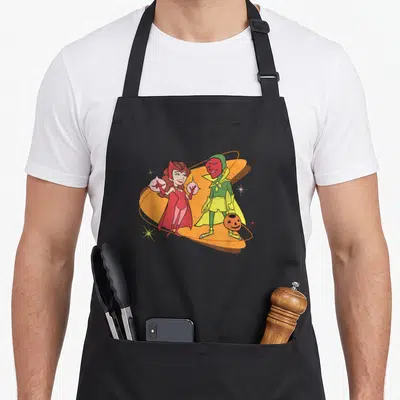 Tablier de cuisine noir avec Wanda en robe rouge et Vision en tenue verte tenant une lanterne d'Halloween sur fond orange.