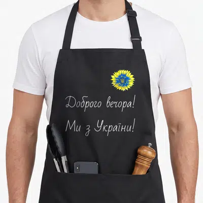 Tablier de cuisine noir orné d'un tournesol stylisé bleu et jaune et de textes en alphabet cyrillique blanc.
