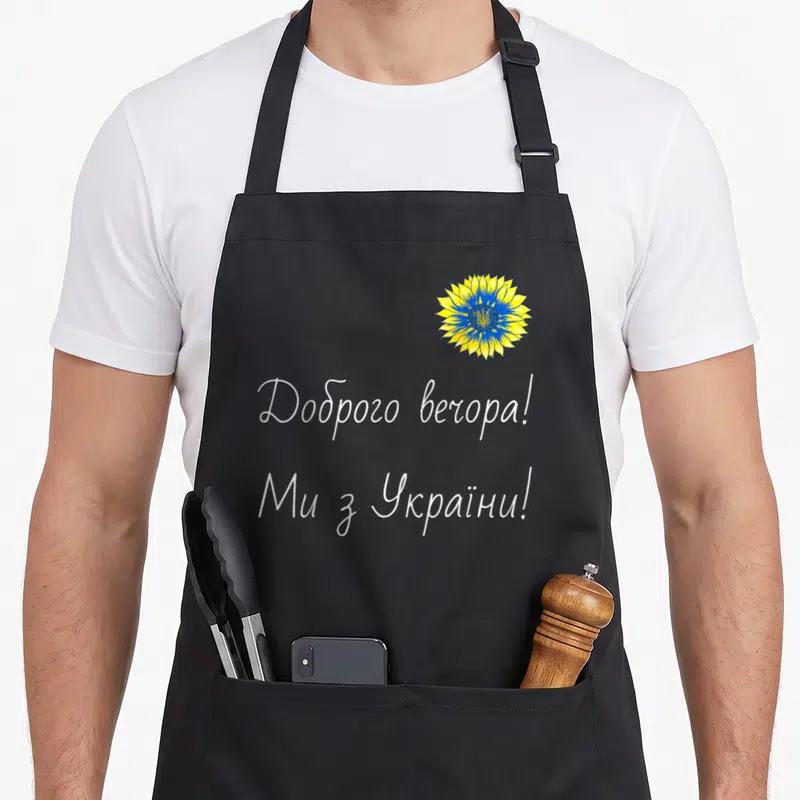 Tablier de cuisine noir orné d'un tournesol stylisé bleu et jaune et de textes en alphabet cyrillique blanc.