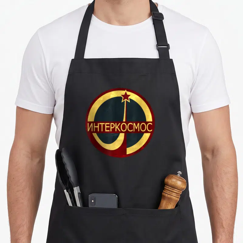 Tablier de cuisine noir avec le logo rond Interkosmos, étoile rouge et lettres dorées cyrilliques.