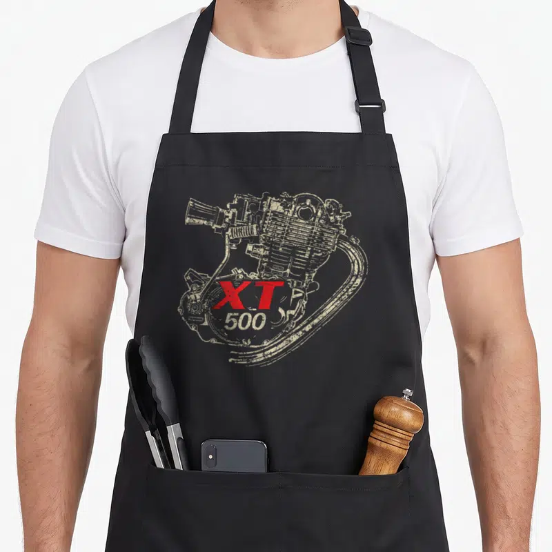 Tablier de cuisine noir avec illustration détaillée d'un moteur XT 500 en tons sépia et texte rouge vif au centre.