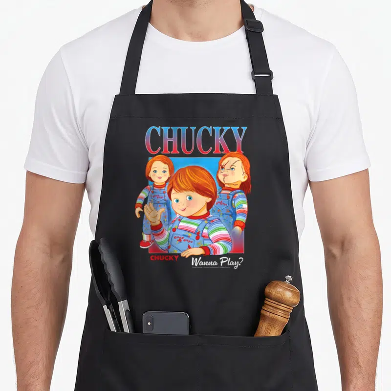 Tablier de cuisine noir avec illustration colorée de Chucky Wanna Play en style vintage années 80.