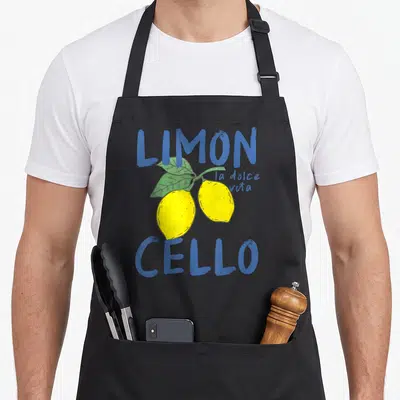 Tablier de cuisine noir avec deux citrons jaunes, des feuilles vertes et le texte Limoncello La Dolce Vita en bleu.