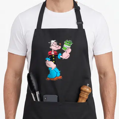 Tablier de cuisine noir avec illustration colorée de Popeye homme marin tenant une boîte d'épinards verte.