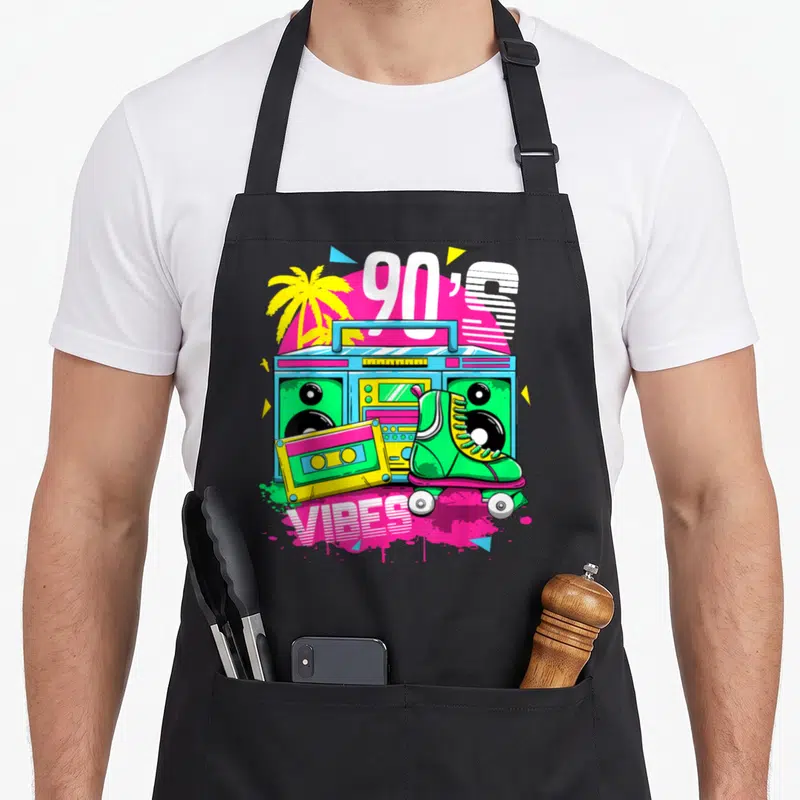 Tablier de cuisine noir avec une illustration colorée d'une boombox, des patins à roulettes et le texte 90's Ambiance en style rétro.