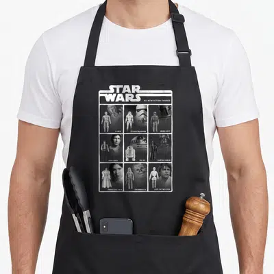 Tablier de cuisine noir avec une illustration rétro montrant Luke, Han, Leia, R2-D2 et d'autres personnages de la saga sous forme de figurines.