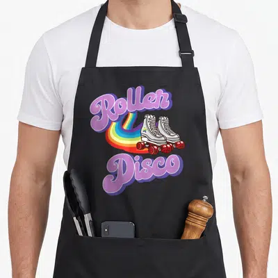 Tablier de cuisine noir avec illustration de patins à roulettes, arc-en-ciel et texte Roller Disco en typographie rétro rose et violette.