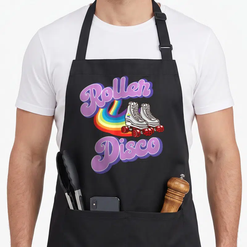 Tablier de cuisine noir avec illustration de patins à roulettes, arc-en-ciel et texte Roller Disco en typographie rétro rose et violette.