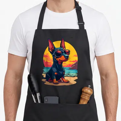 Tablier de cuisine noir avec illustration d'un Doberman Pinscher aux lunettes de soleil sur fond de plage et soleil orange.