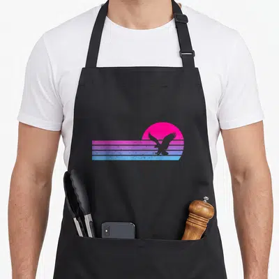 Tablier de cuisine noir avec aigle en silhouette sur fond de soleil rose et bandes horizontales bleues et violettes.