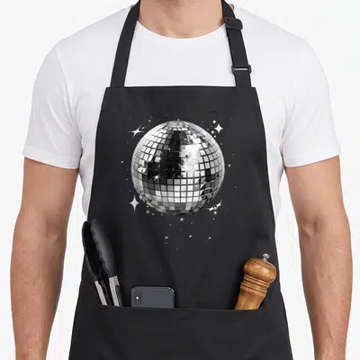 Tablier de cuisine noir avec illustration d'une boule disco miroir argentée entourée d'étoiles scintillantes blanches sur fond uni.