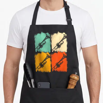 Tablier de cuisine noir avec quatre trompettes dessinées sur des carrés de couleur vert, beige, orange et rouge vif.
