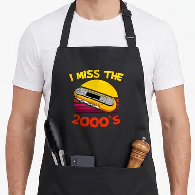 Tablier de cuisine noir avec illustration d'un lecteur MP3 jaune et texte I MISS THE 2000'S sur fond de soleil rétro.