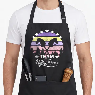 Tablier de cuisine noir avec design rétro Team Hobby Horse, étoiles blanches et silhouettes de chevaux jouets sur fond coloré.
