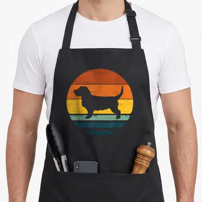 Tablier de cuisine noir avec silhouette basset fauve de bretagne sur fond circulaire orange jaune et bleu style rétro