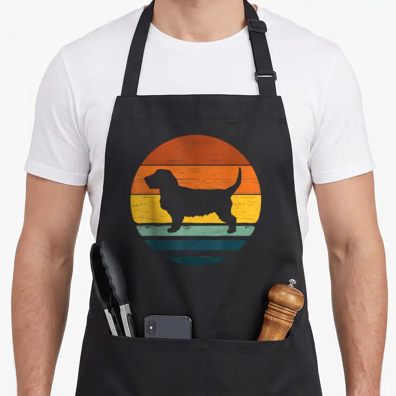 Tablier de cuisine noir avec silhouette basset fauve de bretagne sur fond circulaire orange jaune et bleu style rétro