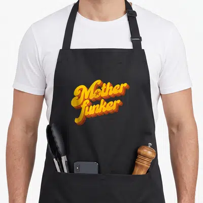 Tablier de cuisine noir avec l'inscription Motherfunker en lettres jaunes et oranges style funk rétro.