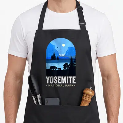 Tablier de cuisine noir avec illustration vintage du parc national de Yosemite montrant des ours et une lune sous un ciel bleu.