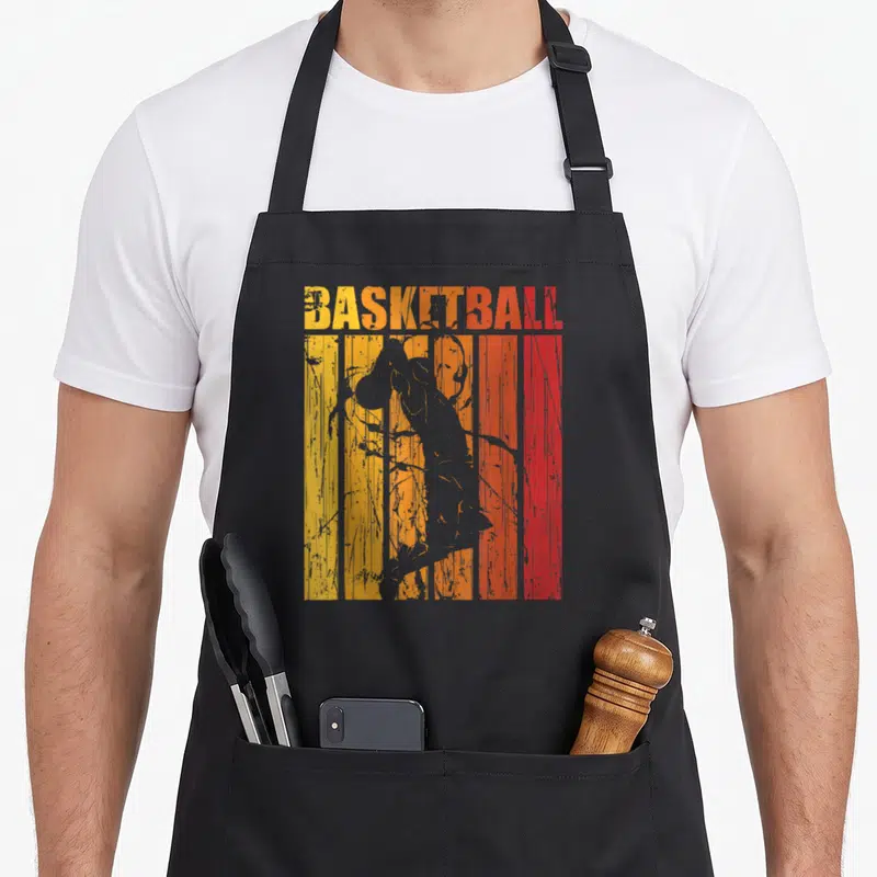 Tablier de cuisine noir avec illustration retro d'un joueur de basket en train de dunker sur fond rayé orange et rouge.