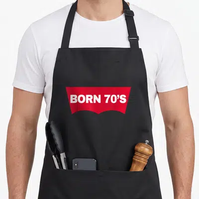 Tablier de cuisine noir avec forme rouge et texte blanc Born 70's au centre.