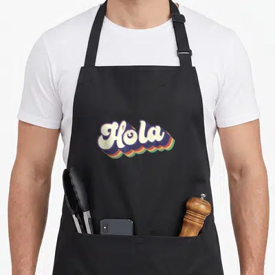 Tablier de cuisine noir avec l'inscription Hola en lettres arrondies multicolores style rétro espagnol mexicain.