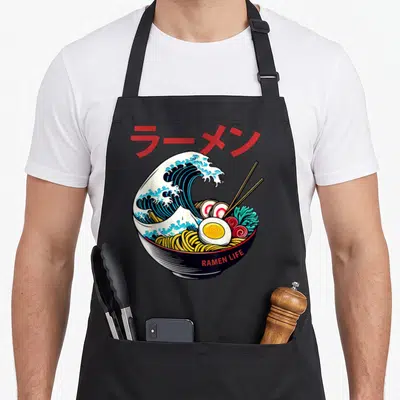 Tablier de cuisine noir avec illustration d'un bol de ramen intégrant une grande vague bleue style Hokusai et des kanjis rouges en haut.