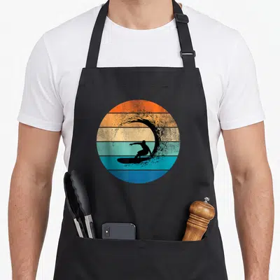 Tablier de cuisine noir avec illustration circulaire d'un surfer sur vague aux couleurs pastel rayées orange et bleu