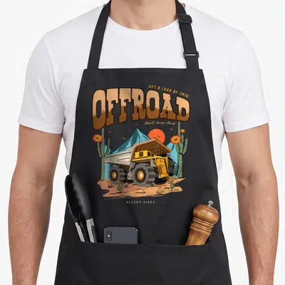 Tablier de cuisine noir avec illustration d'un dumper truck jaune dans un paysage désertique rétro.