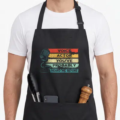 Tablier de cuisine noir avec microphone rétro et bandes colorées affichant Voice Actor You've Probably Heard Me Before.