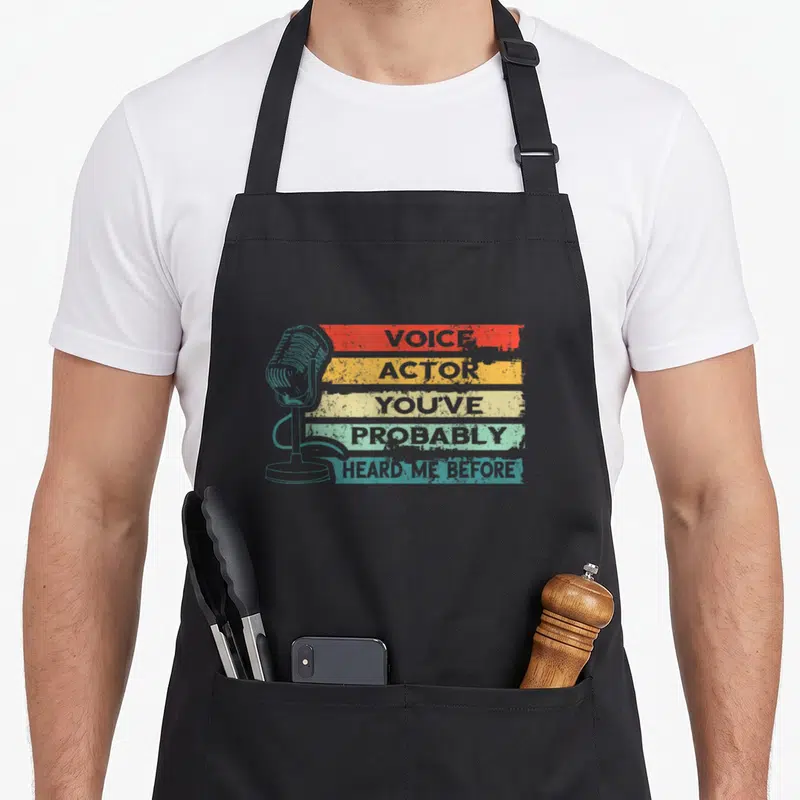 Tablier de cuisine noir avec microphone rétro et bandes colorées affichant Voice Actor You've Probably Heard Me Before.