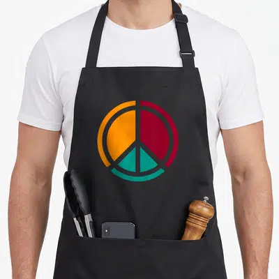 Tablier de cuisine noir avec un panneau rétro coloré Love and Peace en orange, rouge et vert turquoise.