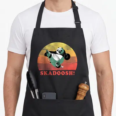 Tablier de cuisine noir avec portrait circulaire du panda Skadoosh en pose d'art martial et texte rouge SKADOOSH en bas.