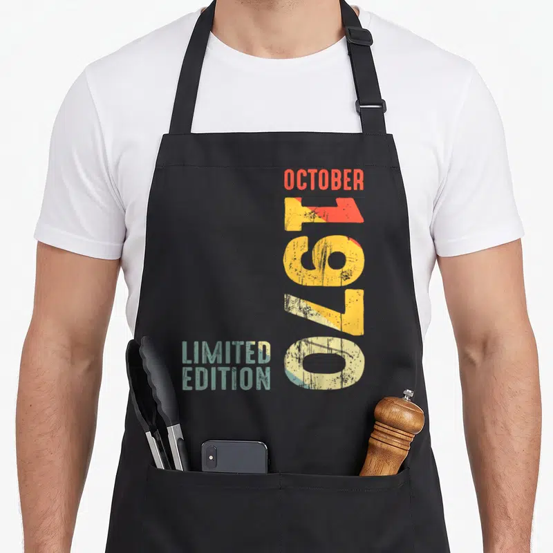 Tablier de cuisine noir avec typographie verticale Octobre 1970 Limited Edition aux couleurs dégradées et effet usé.