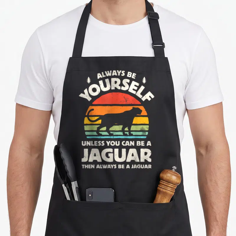Tablier de cuisine noir avec motif rétro Always Be Yourself Jaguar et soleil coloré.