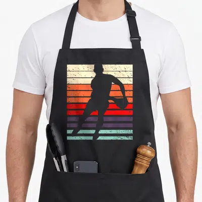 Tablier de cuisine noir avec silhouette de joueur de rugby sur fond de bandes colorées style années 70.