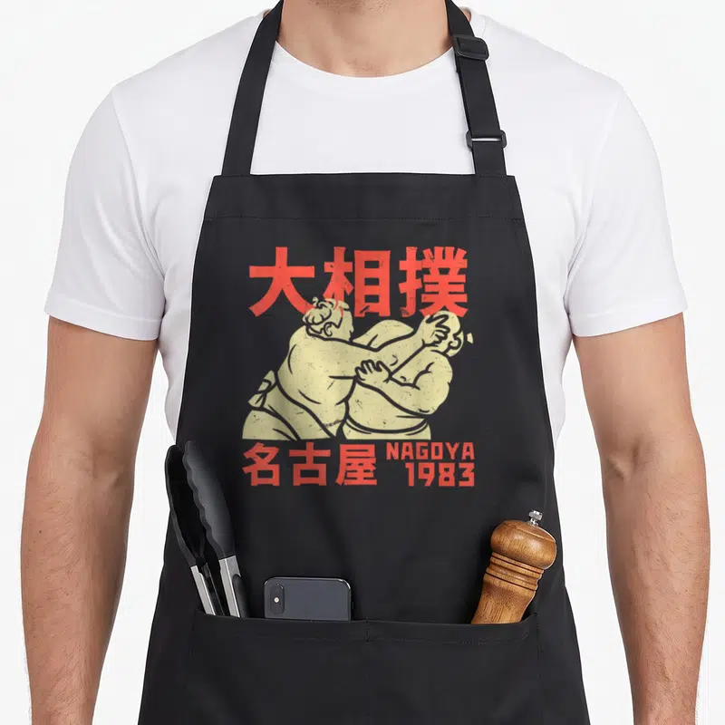 Tablier de cuisine noir avec illustration rétro de lutteurs de sumo et texte rouge Nagoya 1983.
