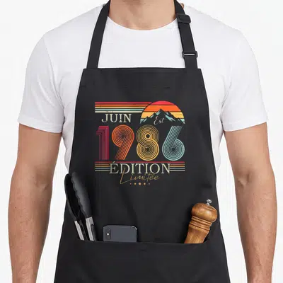 Tablier de cuisine noir avec motif 1986 Juin « Édition Limitée » style rétro et montagnes colorées.