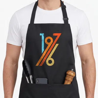 Tablier de cuisine noir avec le motif graphique 1976 aux couleurs vives et effet vieilli.
