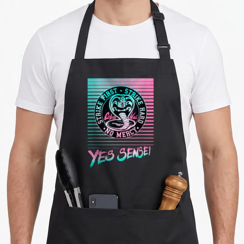 Tablier de cuisine noir avec un logo cobra néon rose et bleu et l'inscription Yes Sensei en bas.