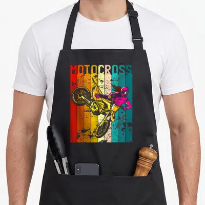 Tablier de cuisine noir avec illustration rétro d'une pilote de motocross sur moto jaune et casque rose devant des bandes de couleur.