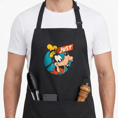 Tablier de cuisine noir avec une illustration de Goofy souriant et le mot Just en rouge sur fond bleu.