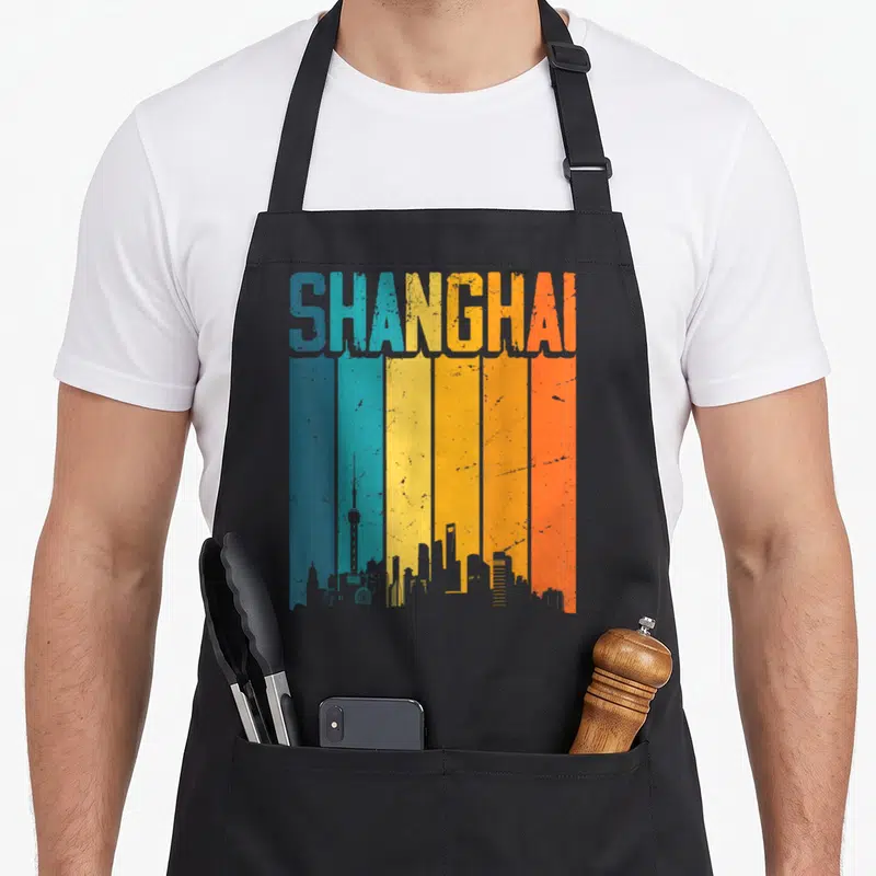 Tablier de cuisine noir avec skyline de Shanghai en bandes colorées et texte SHANGHAI en lettres délavées style rétro.