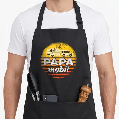 Tablier de cuisine noir avec illustration d'une caravane jaune tirée par un SUV et le texte Papa mobil en blanc sur fond orange délavé.