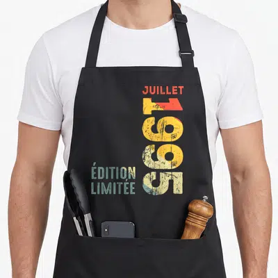 Tablier de cuisine noir avec l'inscription verticale Juillet 1995 en typographie rétro colorée.