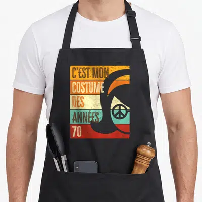 Tablier de cuisine noir avec illustration retro disco et texte C'est mon costume des années 70 sur fond de bandes colorées.