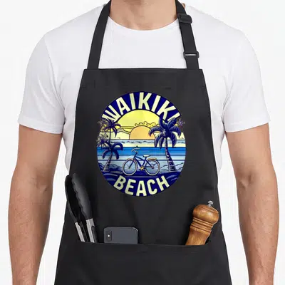 Tablier de cuisine noir avec illustration circulaire Waikiki Beach montrant un vélo et des palmiers au coucher du soleil.